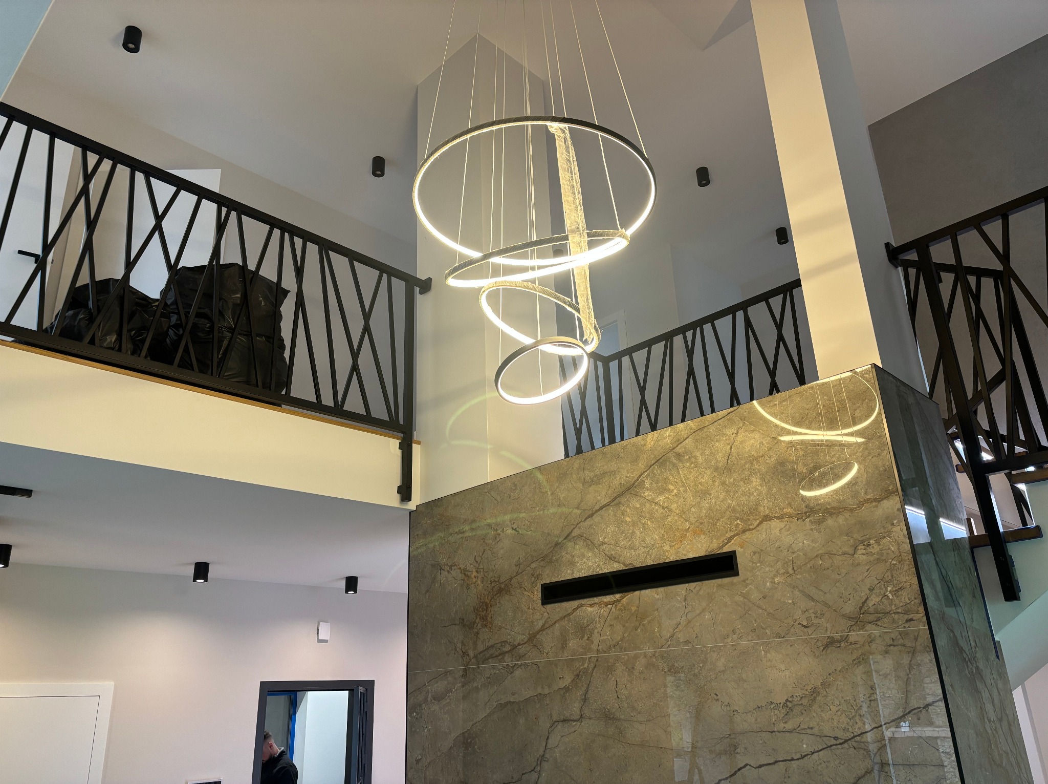 Nowoczesne, czarne balustrady schodowe z geometrycznym wzorem w przestronnym wnętrzu z marmurową ścianą i designerską lampą.