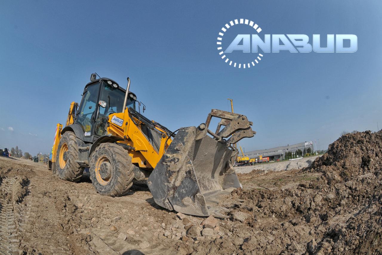 Żółta koparko-ładowarka JCB na placu budowy, z logo firmy ANABUD widocznym na maszynie i w tle na niebie.