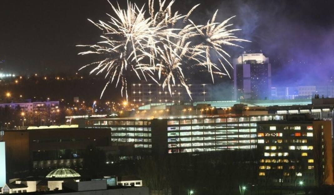 Nocne fajerwerki rozświetlające panoramę miasta z widocznymi budynkami biurowymi i w oddali wzgórzami.