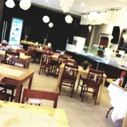 Sala restauracyjna z drewnianymi stołami i krzesłami, udekorowana białymi pomponami, z widoczną tablicą menu i lodówką z napojami w tle.