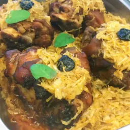 Cztery porcje pieczonej golonki z kapustą, śliwkami i listkami bazylii w metalowej tacy.