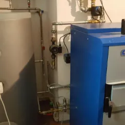 Kocioł na paliwo stałe Ognivo Eko Plus z podłączonym zasobnikiem ciepłej wody, widoczne orurowanie i sterownik elektroniczny na górze kotła.