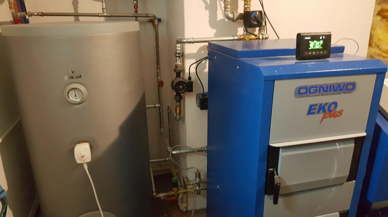 Kocioł na paliwo stałe Ognivo Eko Plus z podłączonym zasobnikiem ciepłej wody, widoczne orurowanie i sterownik elektroniczny na górze kotła.