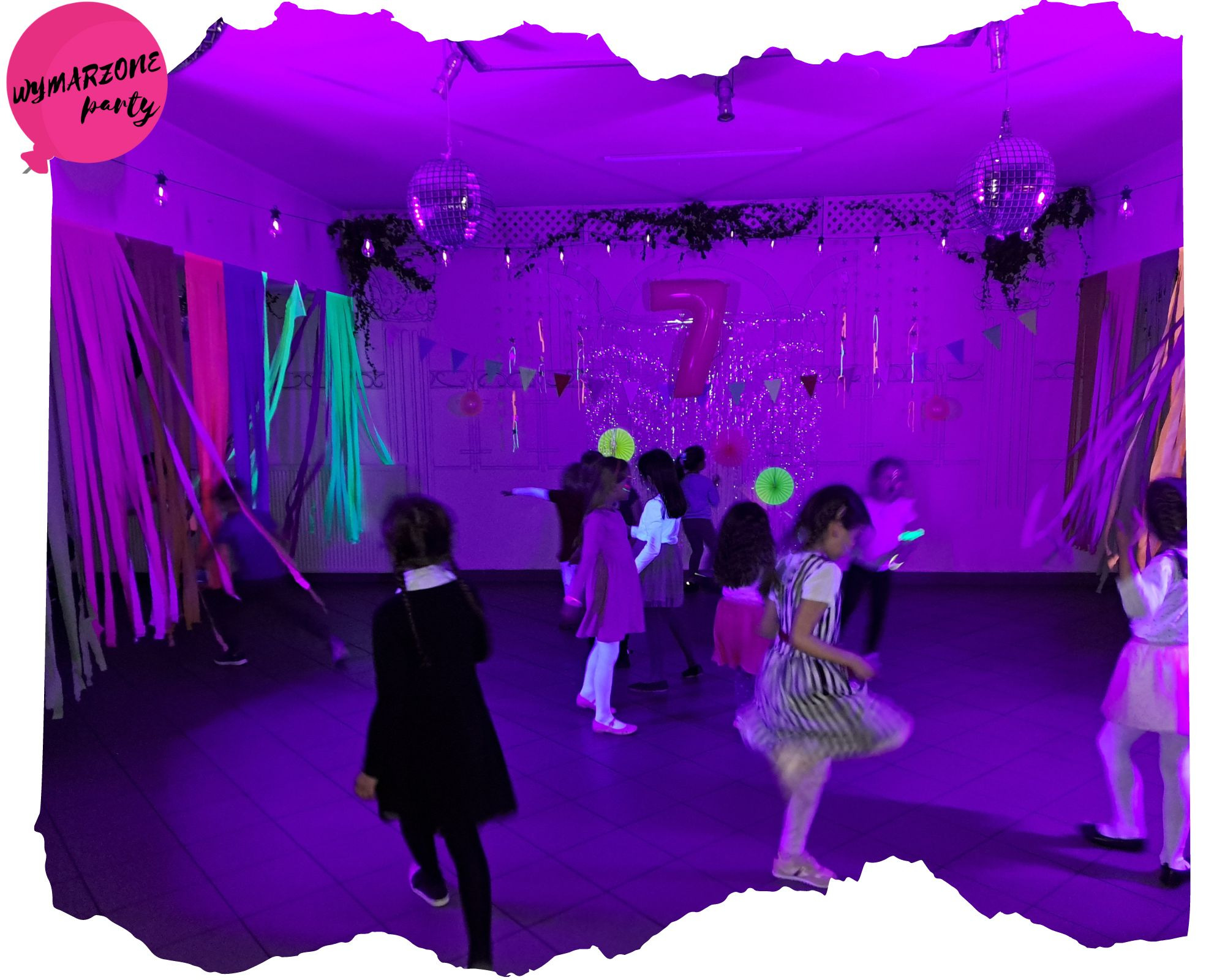 Urodzinowe przyjęcie dla dzieci z dekoracjami, balonem z napisem 'Wymarzone Party' i dyskotekowymi kulami, oświetlone fioletowym światłem.