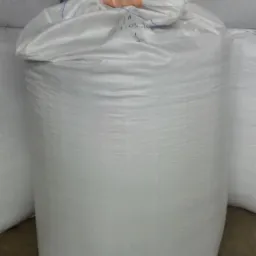 Wielkogabarytowy biały worek z pelletem, z widoczną datą 27.03.20 na górze, ustawiony na betonowej posadzce magazynu, otoczony innymi workami.