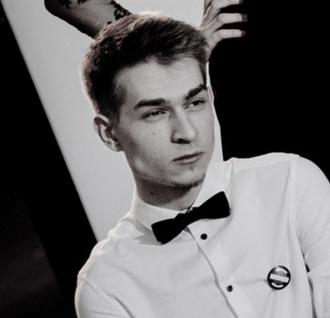 Portret młodego mężczyzny w białej koszuli i muszce, z poważnym wyrazem twarzy, na czarno-białym tle z elementami dekoracyjnymi.