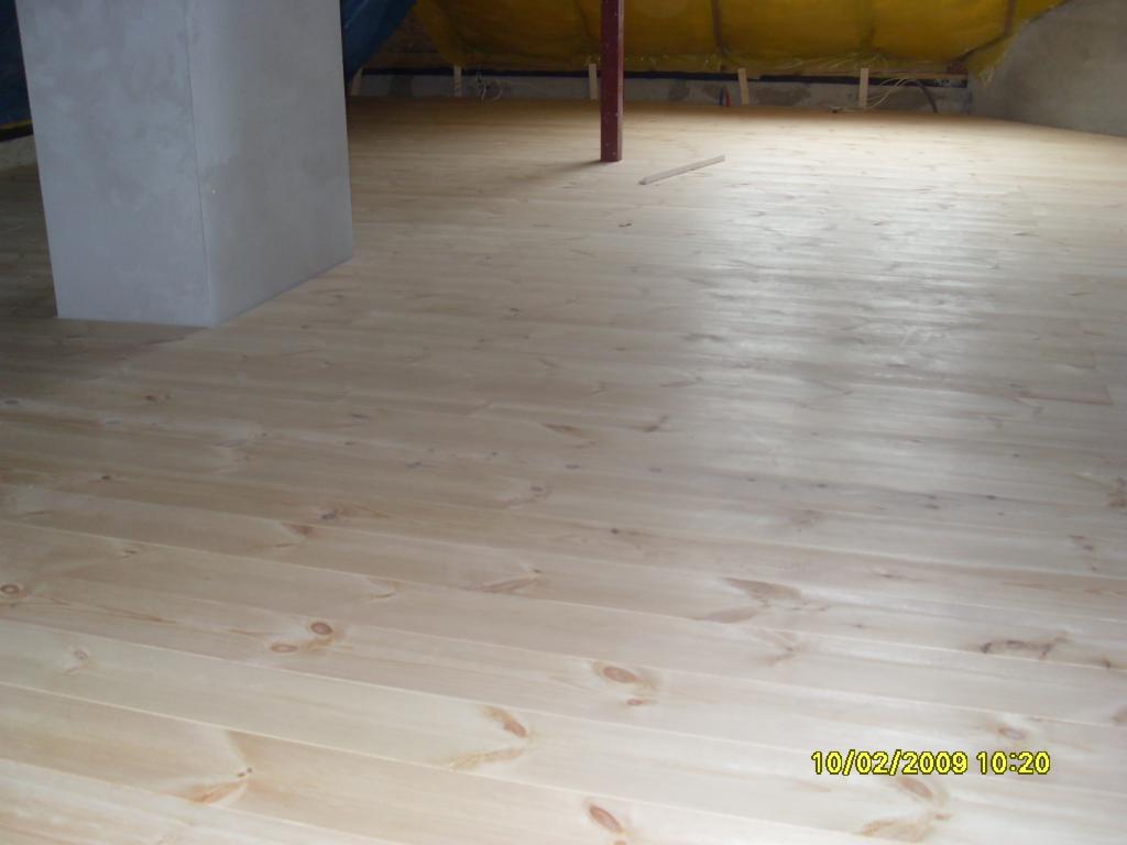 Jasna, świeżo położona drewniana podłoga z widocznym słupem konstrukcyjnym w pomieszczeniu w trakcie wykańczania, z żółtą izolacją widoczną w tle.