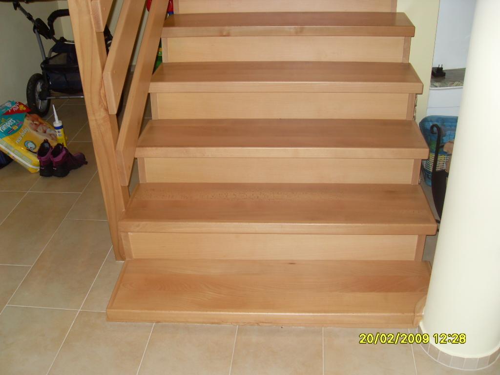 Jasne, drewniane schody z barierką, widoczne z dołu, z torbą pieluch i wózkiem dziecięcym w tle, sfotografowane z datą 20/02/2009.