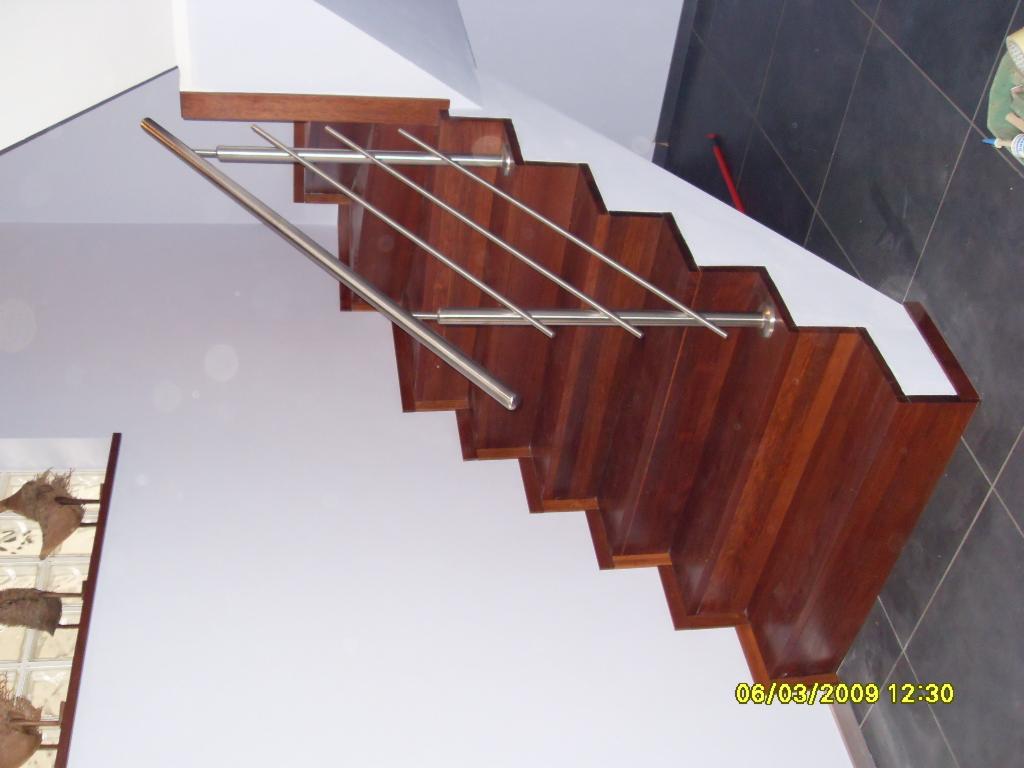 Schody z ciemnego drewna z metalową balustradą, widok z dołu, na ścianie dekoracyjny element z luksferów.