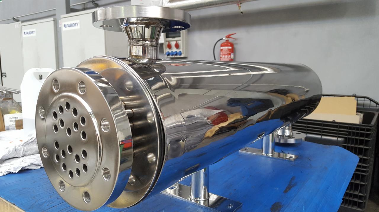 Polerowany, cylindryczny zbiornik ze stali nierdzewnej z perforowaną tarczą na jednym końcu, zamontowany na metalowych wspornikach.