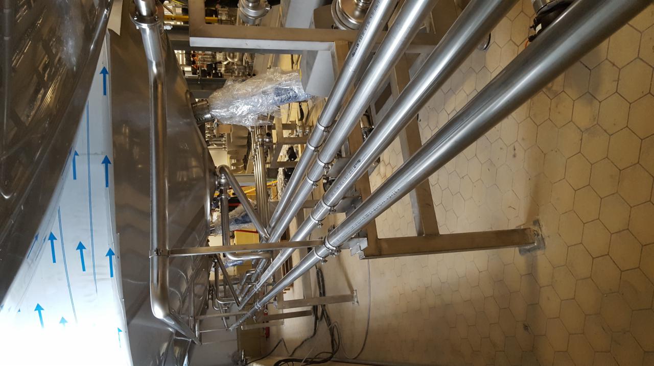Spawane rury ze stali nierdzewnej w instalacji przemysłowej, widoczne elementy montażowe i zbiornik z folią ochronną.