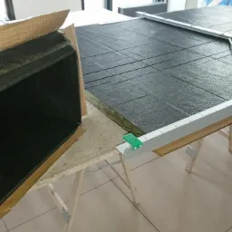 Przygotowany fragment kanału wentylacyjnego z izolacją z wełny mineralnej i okleiną, obok arkusz wełny mineralnej z naniesioną siatką cięć, przycięty narzędziem z miarką.