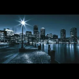 Nocny widok na panoramę miasta z nabrzeża oświetlonego latarnią, odbijającego się w wodzie.