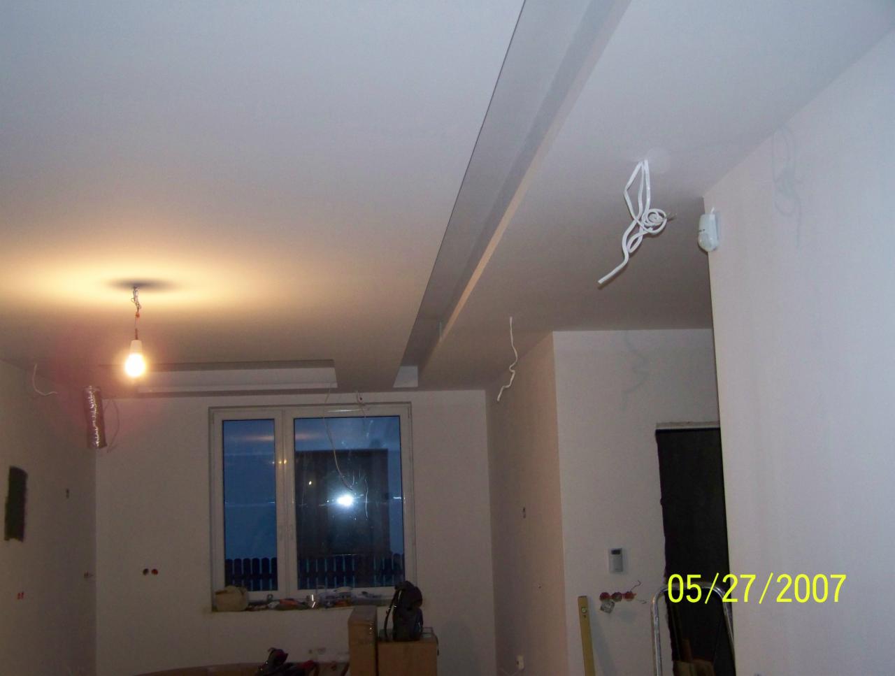 Remontowane wnętrze z podwieszonym sufitem z widocznymi przewodami, surową żarówką i datą na ścianie.