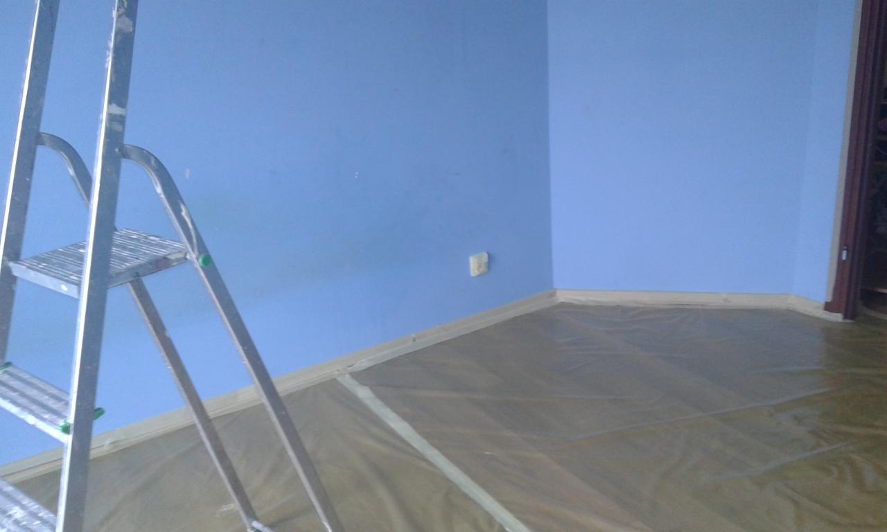 Pokój z pomalowanymi na niebiesko ścianami, zabezpieczoną folią podłogą i aluminiową drabiną malarską.