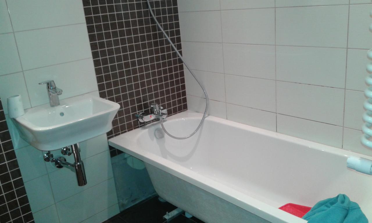 Nowoczesna łazienka z białą wanną, umywalką na postumencie i mozaiką w odcieniach brązu, widok z niskiej perspektywy.