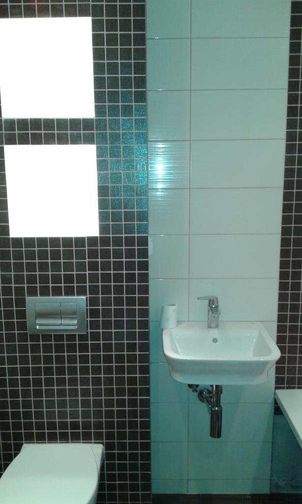 Nowoczesna łazienka z czarno-białą mozaiką, umywalką nablatową i chromowaną armaturą, widoczny fragment toalety.