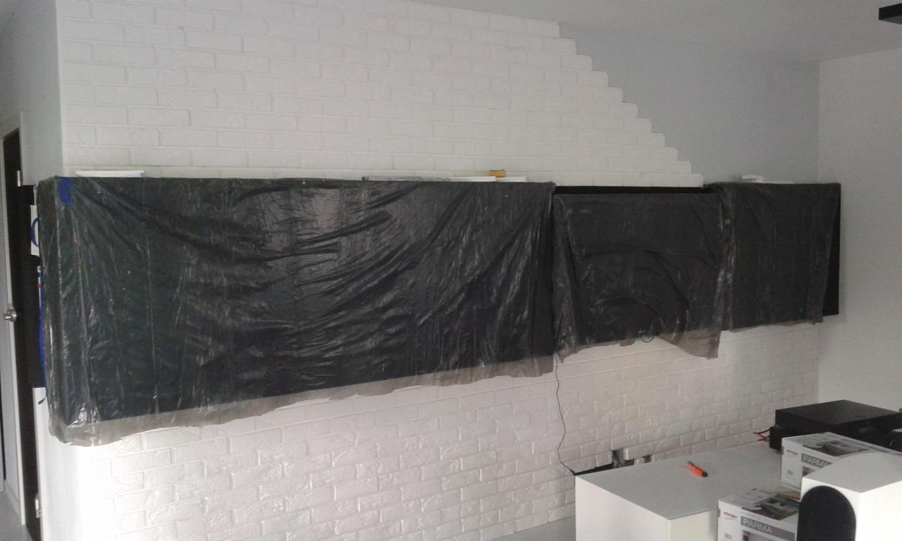 Przygotowanie ściany z białej cegły do montażu szafek wiszących, zabezpieczonych folią ochronną, widoczne elementy wyposażenia wnętrza.