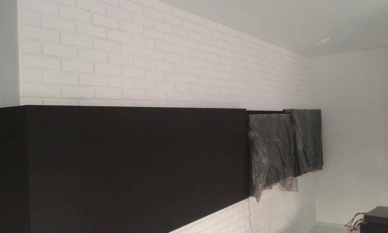 Częściowo pomalowana ściana z cegły na biało, z czarną farbą na dole i zabezpieczonymi folią dwoma elementami na ścianie.