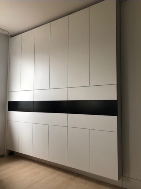 Biała zabudowa ścienna z czarnym, poziomym pasem pośrodku, obejmująca górne i dolne szafki z prostymi frontami.