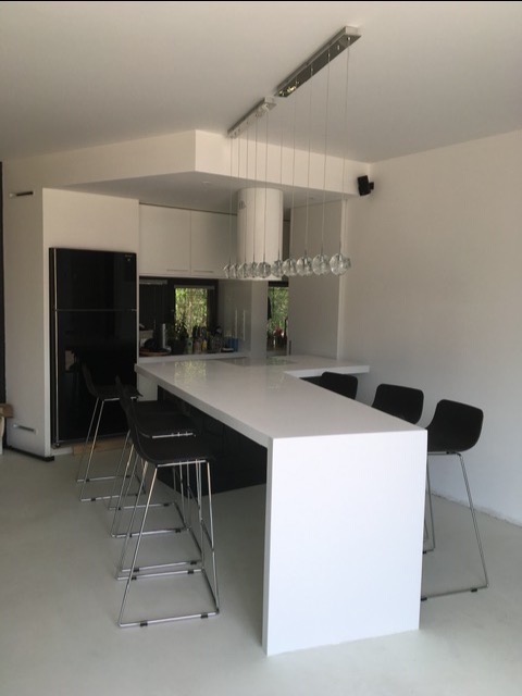 Nowoczesna, biała kuchnia z wyspą i czarnymi hokerami, oświetlona wiszącą lampą z kryształowymi kulami.