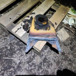 Serwis spawalniczy Piotr Kaźmierczak - Żółta, metalowa konstrukcja z widocznymi śladami spawania, leżąca na drewnianej palecie na tle ziemi i śmieci.