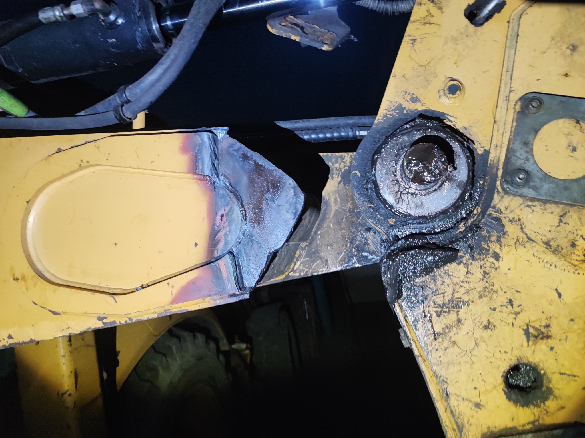 Zbliżenie na połączenie spawane, mocno zużyte ramię maszyny budowlanej, widoczne ślady smaru i pęknięcia.