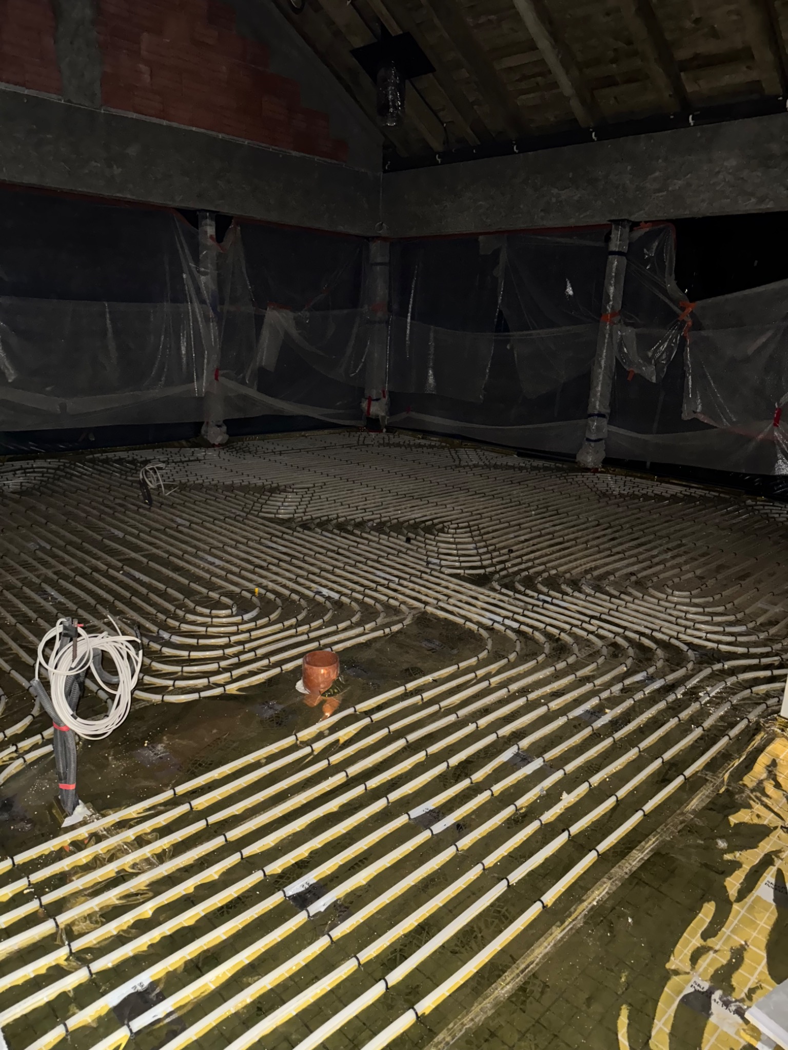 Instalacja ogrzewania podłogowego w trakcie realizacji: białe rurki układane w pętle na folii izolacyjnej, widoczne elementy mocujące i przygotowane przewody.