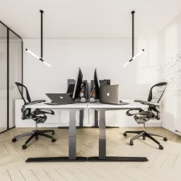 Nowoczesne stanowiska pracy w biurze z regulowanymi biurkami, ergonomicznymi krzesłami, laptopami i monitorami, oświetlone minimalistycznymi lampami wiszącymi.