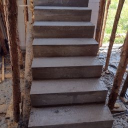 SPRINT-BUD Zbigniew Koloch - Surowe, betonowe schody zewnętrzne w trakcie budowy, widoczne drewniane podpory szalunku i fragment ściany z bloczków.