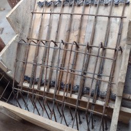 SPRINT-BUD Zbigniew Koloch - Zbrojenie w szalunku z desek, widoczne elementy konstrukcyjne i plastikowe dystanse, przygotowane do zalania betonem.