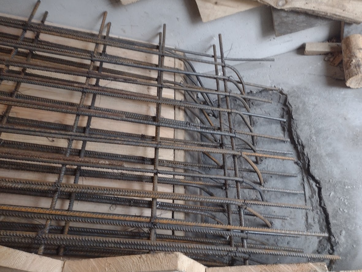 Siatka zbrojeniowa ułożona na deskach szalunkowych, częściowo zalana betonem, widoczne pęknięcie betonu.