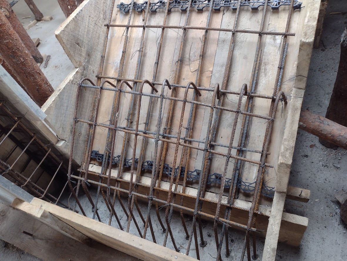 Zbrojenie w szalunku z desek, widoczne elementy konstrukcyjne i plastikowe dystanse, przygotowane do zalania betonem.