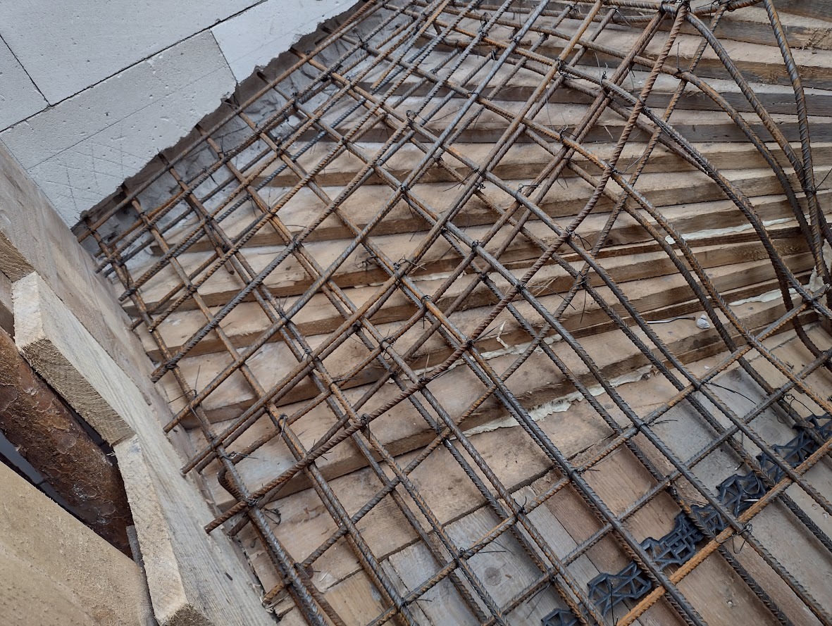 Siatka zbrojeniowa ułożona na drewnianym szalunku, widoczne dystanse z tworzywa sztucznego, przygotowanie do wylania betonu.