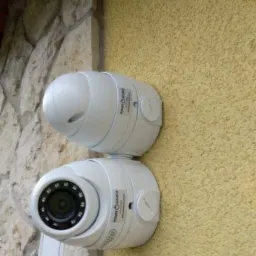 Dwie kamery monitoringu Dahua zamontowane na styku ściany z kamienia i ściany o żółtej, chropowatej fakturze, widoczne etykiety i diody IR.