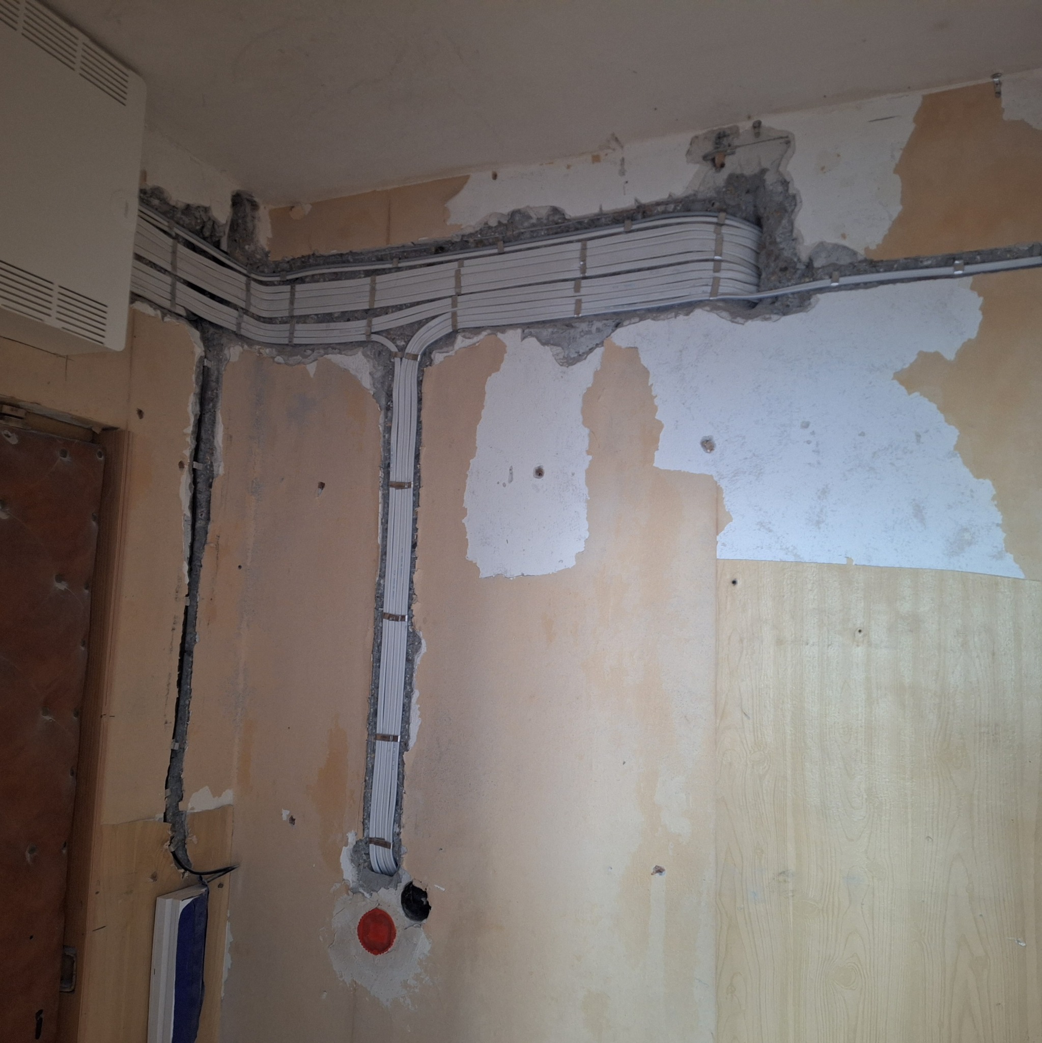 Przewody elektryczne prowadzone w korytach ściennych, ściana w trakcie remontu, widoczne ślady po kuciu i starej farbie.