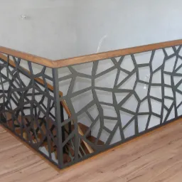 Nowoczesna balustrada schodowa z geometrycznym wzorem, drewnianym wykończeniem i widocznymi schodami w tle.
