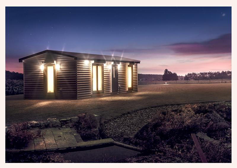 Nowoczesny, parterowy budynek z drewnianych bali oświetlony ciepłym światłem w nocy, z widocznym kamiennym murkiem i fragmentem strumyka w tle.