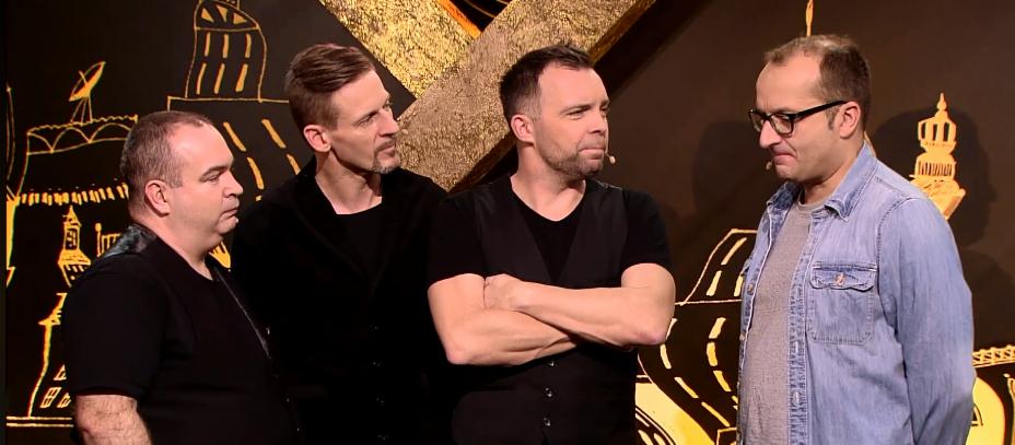Czterej mężczyźni w różnym wieku stoją na scenie przed czarnym tłem z abstrakcyjnymi złotymi rysunkami, dwóch z nich ma mikrofony przypięte do koszul.