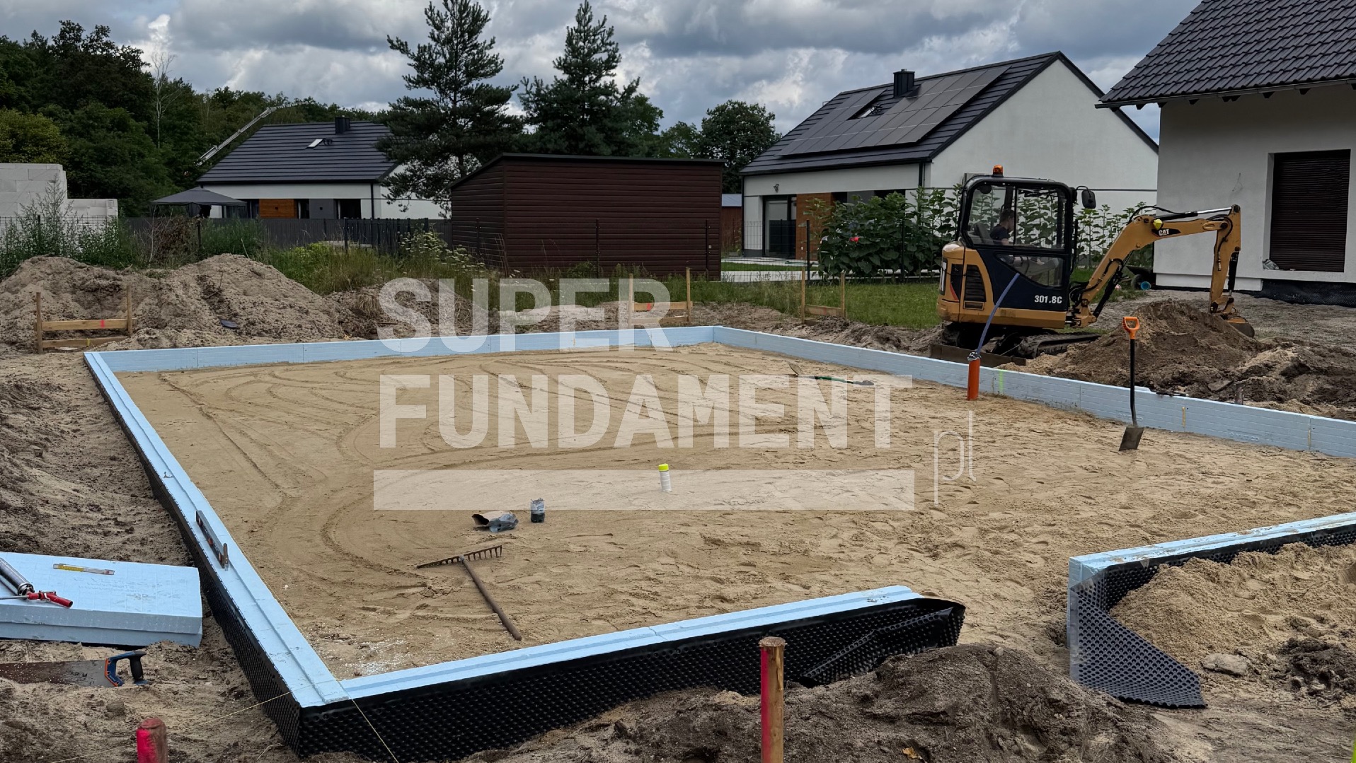 Przygotowany teren pod wylewkę fundamentów z izolacją termiczną i mini koparką w tle, widok na budowę domu jednorodzinnego.