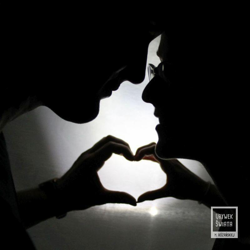Silhouettes of a couple forming a heart with their hands against a bright background, with a logo in the corner.