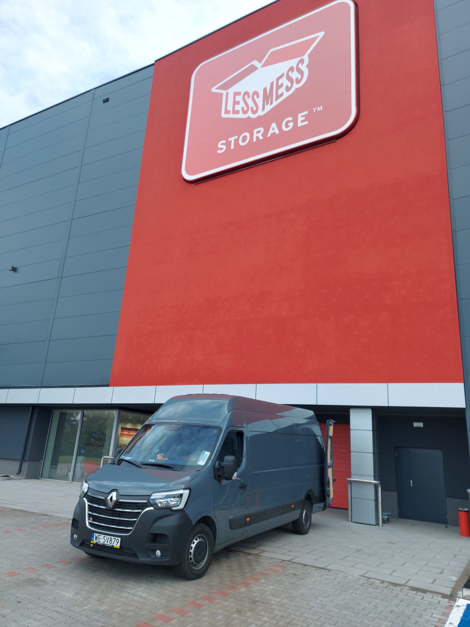 Szary bus Renault Master zaparkowany przed budynkiem magazynu samoobsługowego Less Mess Storage z otwartymi drzwiami tylnymi.