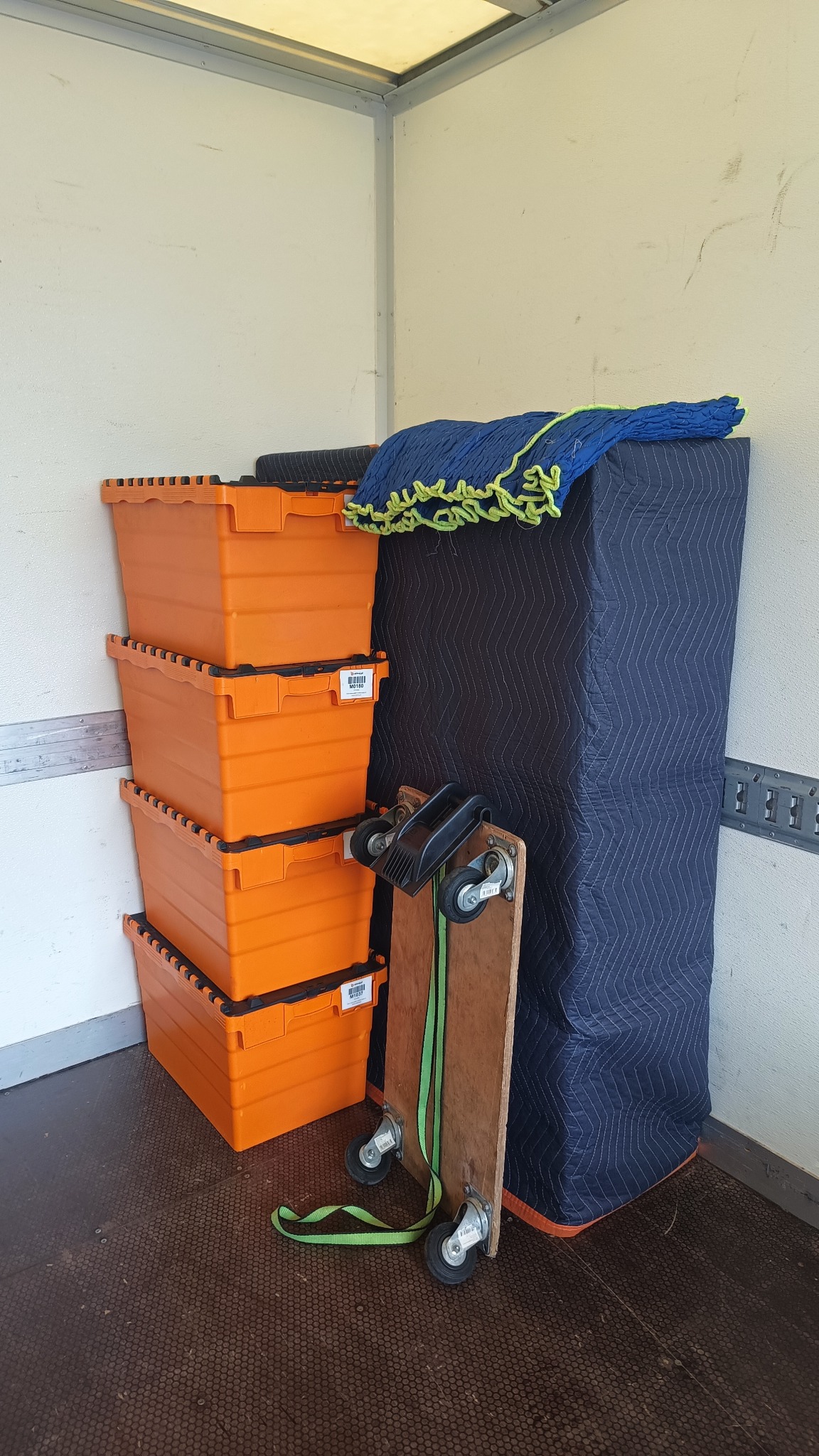 Stos pomarańczowych pojemników, wózek transportowy i zabezpieczony kocem mebel wewnątrz pojazdu dostawczego. Sprzęt do przewozu rzeczy.