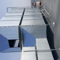 Rozbudowany system kanałów wentylacyjnych na dachu budynku w Ostrowie Wielkopolskim, widoczne elementy mocujące i drabina serwisowa.