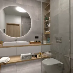 Nowoczesna łazienka z okrągłym lustrem podświetlanym LED, umywalką nablatową i szarymi płytkami imitującymi beton, widoczna kabina prysznicowa za szybą.