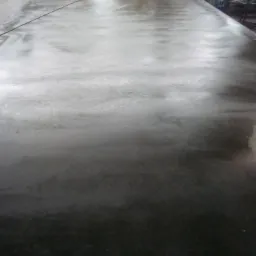 Świeżo wylana, mokra posadzka przemysłowa w hali z widocznymi śladami po narzędziach i przewodzie na powierzchni.