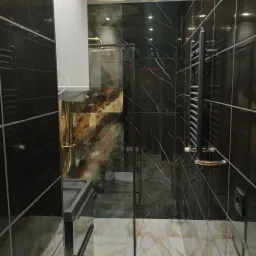 Nowoczesna łazienka z czarnymi płytkami imitującymi marmur z białymi żyłami, grzejnikiem drabinkowym w kolorze grafitowym i szklaną kabiną prysznicową.