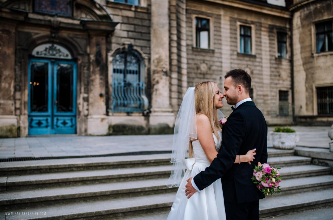 Para młoda w objęciach na tle schodów i zabytkowej fasady budynku z niebieskimi drzwiami.