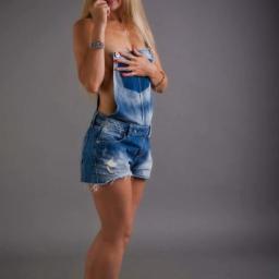 Viktoriiamodels - Portret kobiety z blond włosami, ubranej w dżinsowe ogrodniczki, pozującej na szarym tle w studio.