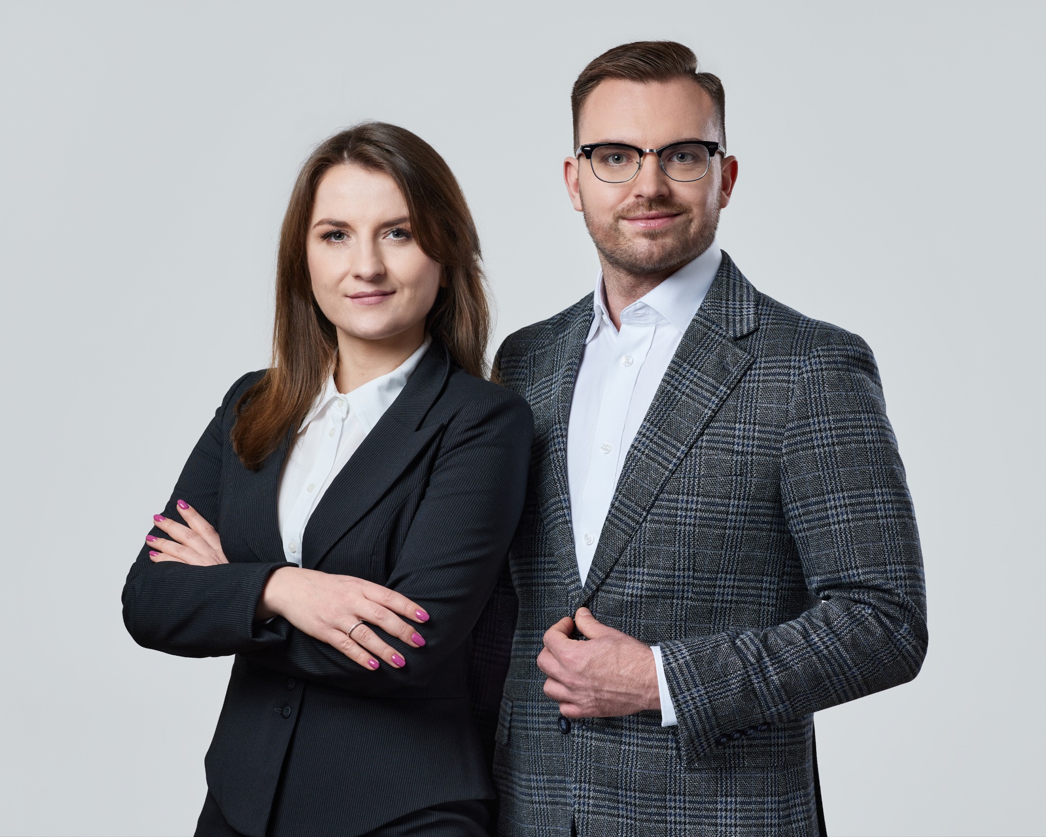 Portret kobiety z założonymi rękami i mężczyzny w kraciastej marynarce, prezentujący profesjonalizm biura rachunkowego lub doradcy podatkowego na jasnym tle.